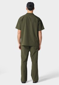 Camisa de manga corta verde oliva y pantalones a juego, con una textura suave, corte recto y un sutil logotipo en la parte posterior.