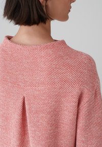 Maglione a maglia testurizzata di colore rosa chiaro, con taglio morbido, scollatura rotonda e leggera trama orizzontale. Presenta una piega centrale sul retro.