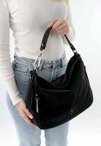 Schwarze Handtasche aus strukturiertem Stoff, mit geschwungener Form, silbernem Zubehör und einem hängenden Quastenakzent. Verstellbarer Schultergurt inklusive.
