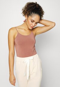 Top ajustado rosa com alças finas, combinado com calças de moletom em tom creme com cordão branco. Tecido suave e leve.