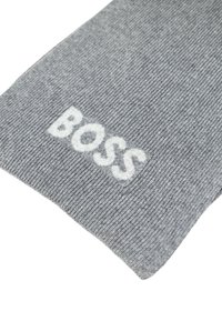 Světlá šedá žebrovaná šála s bílým vyšitým logem "BOSS" na jednom konci. Materiál se zdá být měkký s texturovaným povrchem.