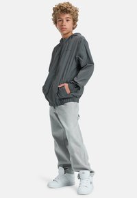 Grå lättviktsjacka med huood och elastiska ärmar, paired med ljusgrå jeans och vita högskor. Enkelt design, inga mönster.