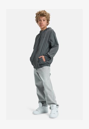 Grau leichte Kapuzenjacke mit elastischen Bündchen, kombiniert mit hellgrauen Jeans und weißen hochfrontigen Sneakers. Einfaches Design, keine Muster.
