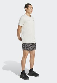 Chemise courte en beige clair à manches courtes avec un logo rose, accompagné d'un short noir avec un motif gris subtil. Des chaussures de sport noires terminent le look.