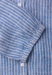 Manche de chemise à rayures verticales bleu et blanc avec poignet élastique et bouton blanc sur fond de tissu rayé assorti.