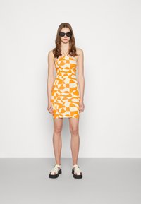 Vestido mini com padrão laranja e branco, com decote halter; combinado com sandálias chunky em creme. A modelo usa óculos de sol pretos.