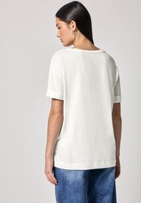 Weißes Kurzarm-T-Shirt mit umgeschlagenen Ärmeln, lässiger Passform und glatter Textur, kombiniert mit blauen Jeans.