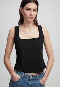 Top senza maniche nero con scollatura quadrata, realizzato in un tessuto liscio, abbinato a jeans in denim blu a vita alta con una texture sbiadita.