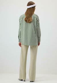 Cămașă cu dungi verzi și albe, cu mâneci lungi, combinată cu pantaloni bej deschis, cu croială lejeră și textură moale. Bentiță albă împletită.