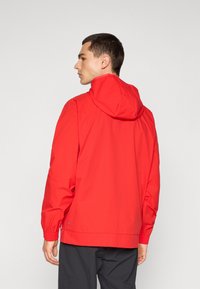 Rød, letvægtet hættejakke med elastiske manchetter og et slankt design, vist fra bagsiden. Inkluderer subtil branding nær sømmen.