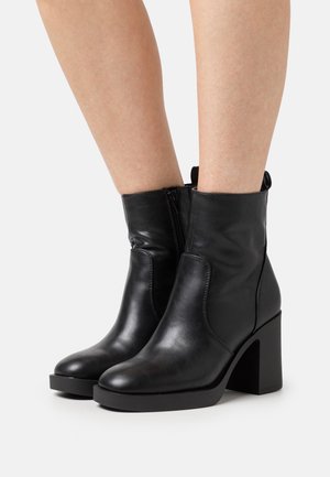 Bottes basses en cuir noir avec un bout arrondi, une fermeture éclair latérale et un talon épais avec une semelle texturée. Finition lisse, design minimaliste.