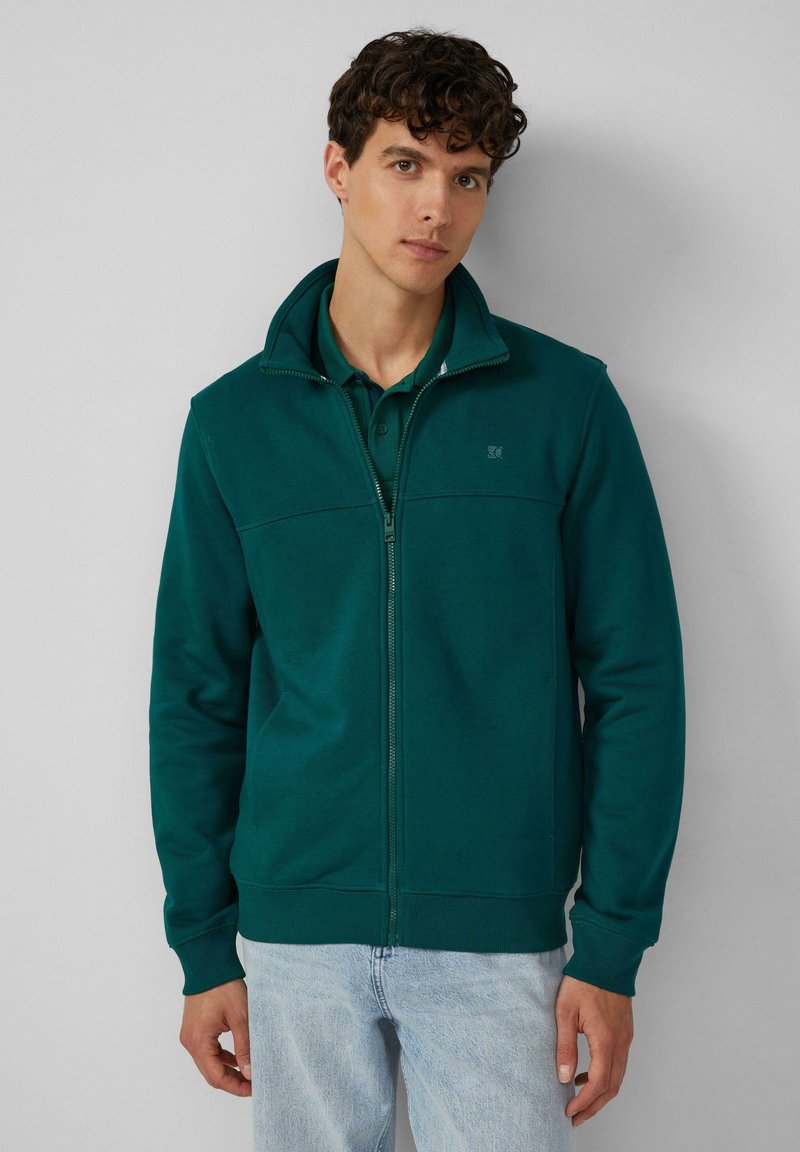 Grüne Kapuzenjacke mit hohem Kragen, aus weichem Stoff gefertigt, mit einem Frontdesign, seitlichen Taschen und gerippten Bündchen.
