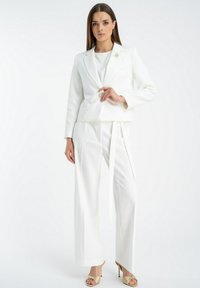 Biały elegancki żakiet z klapami, w połączeniu z szerokimi białymi spodniami z bocznym wiązaniem. Gładka tkanina, minimalne wykończenie, elegancki design.