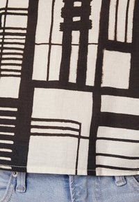 Tejido en blanco y negro con un patrón de líneas audaces y formas geométricas, con una textura suave, bordes cosidos y superpuesto sobre denim azul.