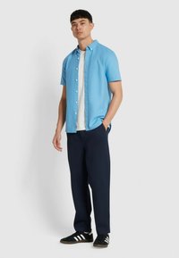 Lichtblauw short-sleeve overhemd met knopen, gecombineerd met een witte T-shirt en marineblauwe broek. Zwarte sneakers met witte strepen maken de outfit compleet.