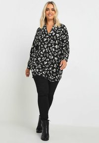 Blusa nera con motivo floreale bianco, scollatura a V e maniche lunghe, abbinata a jeans skinny neri e stivaletti. Tessuto dalla texture liscia.