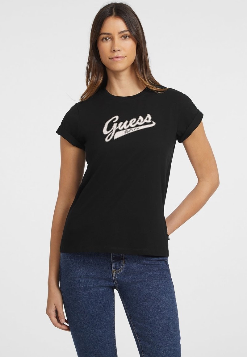 Czarny bawełniany t-shirt z białym logo "Guess Jeans 1981" w kursywie. Krótkie rękawy z podwiniętymi mankietami, okrągły dekolt i dopasowany krój.