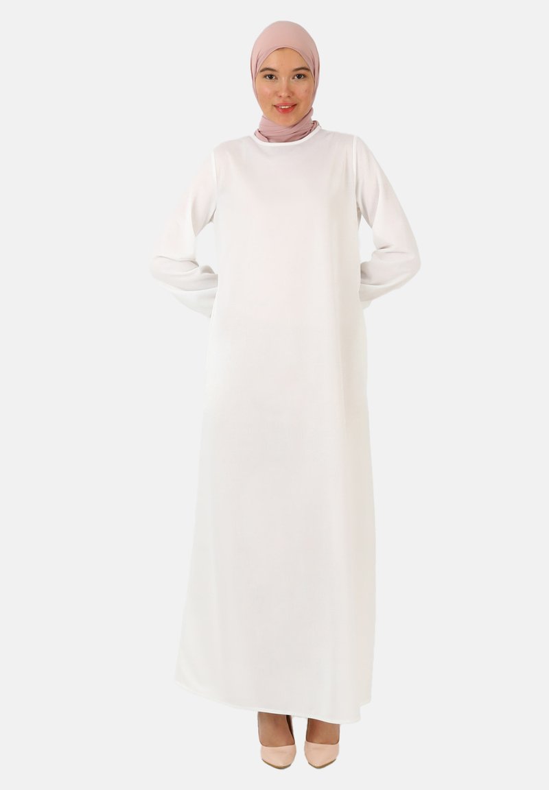 Hvid, langærmet kjole med høj halsudskæring og afslappet pasform, lavet af glat stof. Sammen med en lys pink hijab og nude hæle.