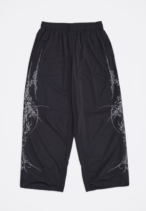 Schwarze, weit geschnittene Netz-Hose mit elastischem Bund und weißen abstrakten Linienkunst-Designs an den Seiten vor weißem Hintergrund.