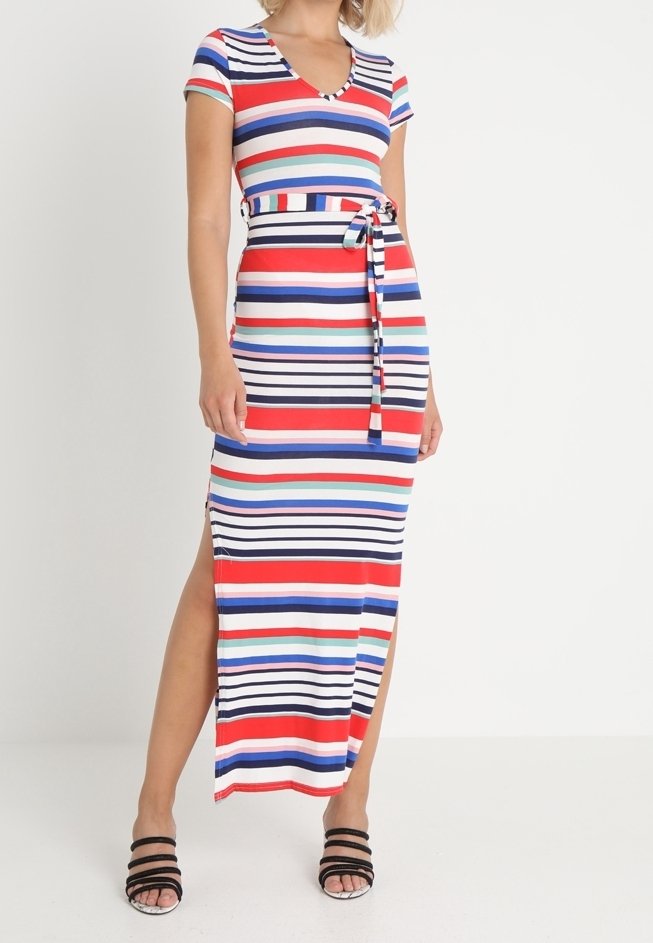 Femme portant une robe maxi à manches courtes, rayée multicolore, avec des fentes latérales et une ceinture assortie, associée à des sandales noires à lanières.