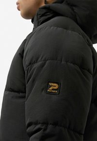 Černá péřová bunda s kapucí, prošívanou texturou a zlatě zvýrazněnou značkovou nášivkou na levém rameni. Hladký, lehký materiál.