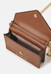 Lille brune læder crossover taske med guld kæde rem, guld trykknap og beige inderside med "Made in China" mærke.