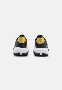 Black and gold athletic shoes with a padded collar, textured material accents, and a white sole featuring distinct tread patterns.