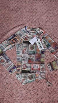 Långärmad skjorta med heltryck av vintageetiketter i olika färger. Har rund halsringning och etikett fastsatt. Materialet verkar vara lätt.