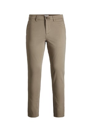 Barn iført lyseblå sweatshirt, beige bukser og hvide sneakers, stående med den ene hånd i lommen mod en ensfarvet baggrund.