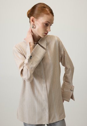 Beżowa koszula w paski wykonana z lekkiego materiału, z kołnierzykiem, długimi rękawami z szerokimi mankietami oraz błyszczącymi akcentami wzdłuż pasków.