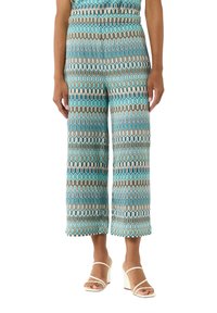 Spodnie culotte w kolorze turkusowym w wzory faliste. Elastyczny pasek w talii i krótka długość. Połączone z białymi sandałami na słupku.