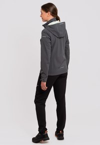 Giacca softshell grigia con cappuccio, con una fodera interna di colore chiaro, abbinata a pantaloni neri e scarpe nere robuste.