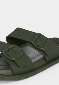 Sandale slide vert foncé avec deux brides réglables à boucle et semelle texturée, présentée sur un fond clair.