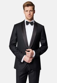 Czarna marynarka smokingowa z satynowymi klapami, zestawiona z białą koszulą i czarnym muszkietem. Dopasowany krój z guzikami na rękawach.
