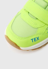 Chaussure de sport verte avec tige synthétique texturée, bride à scratch et semelle en caoutchouc. Marquage bleu "TEX" notable sur le côté.