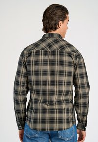 Schwarz-beige karierte Hemd mit langen Ärmeln, durchgehender Knopfleiste und spitzem Kragen. Weiche Textur mit ausgeprägten Karos und minimalistischer Gestaltung.