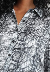 Camicia a motivo di pelle di serpente in bianco e nero con colletto, chiusura a bottoni e texture del tessuto liscia.
