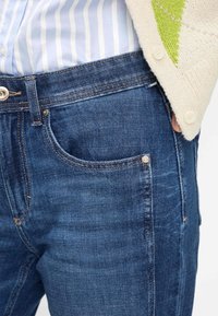 Donkerblauwe spijkerbroek met een klassieke snit, voorzien van een zilveren knoop, contrasterende stiksels en een voorzak.