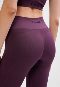 Lila högmidjade leggings gjorda av texturerat tyg, med en slät yta och logotypdetaljer vid midjan.