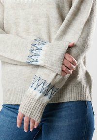 Hellbeige gestrickter Pullover mit langen, gerippten Ärmeln, die an den Bündchen mit blauen geometrischen Mustern verziert sind. Weiche Textur und lockere Passform.