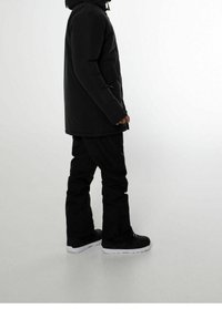 Mustat eristetyt takit, joissa on huppu, sivutaskut ja joustavat hihansuut, yhdistettynä mustiin housuihin ja mustiin tennareihin, joissa on valkoiset pohjat.