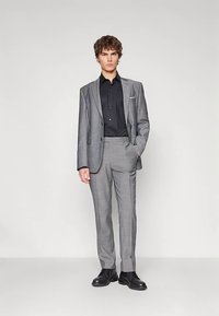 Pilka languota kostiumas su pritaikyta forma, derinamas su juoda marškinėliais. Yra vienos eilės švarkas ir poliruoti juodi batai.