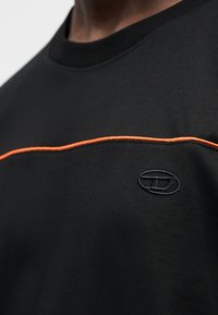 Μαύρο κοντομάνικο πουκάμισο με πορτοκαλί οριζόντια ραφή και κεντημένο λογότυπο σε μαύρο χρώμα. Λείο ύφασμα με σχεδιασμό λαιμόκοψης.