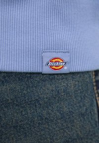 Light blue ribbed fabric with a Dickies logo tag, paired with dark denim, showcasing contrast in color and texture.