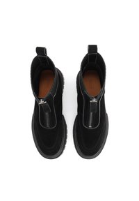 Botas de tobillo de ante negro con cierre de cremallera en la parte delantera, tejido texturizado, suela de goma gruesa y tirador en la parte trasera para facilitar el calzado.