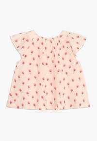 Korte mouwen kindertop in lichtroze stof, met een bloempatroon van kleine rode bloemen en zwarte accenten, met een geplooide halslijn.