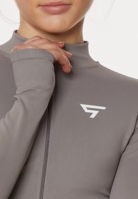 Gray athletic half-zip top with a high collar and fitted design, featuring a logo in white on the chest and long sleeves.
