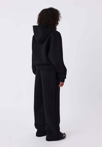 Zwarte oversized hoodie met capuchon en bijpassende wijde sweatpants. Gemaakt van zachte stof met geribbelde boorden en een ontspannen pasvorm.