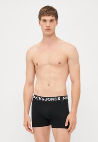 Schwarze Boxer-Shorts mit einem weißen, gebrandeten Bund. Der Stoff wirkt glatt, das Design ist eng anliegend, mit kurzer Beinlänge und minimalen Nähten.