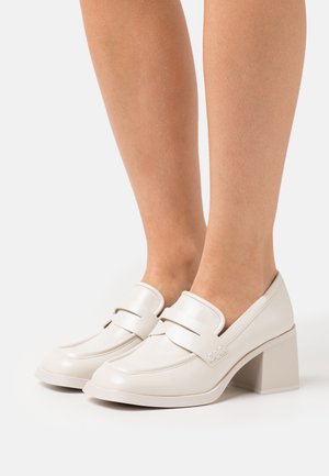 Mocassins en cuir verni blanc avec un bout arrondi, des détails de couture surélevés et un talon carré. Texture lisse et design minimaliste.